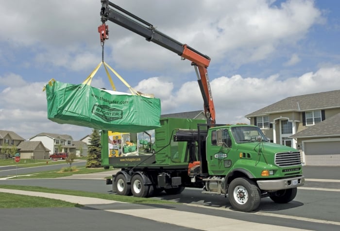 A truck hauling a Bagster away from a home